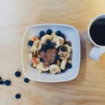 sliced bananas with berries and peanut butter beside cup of coffee on table